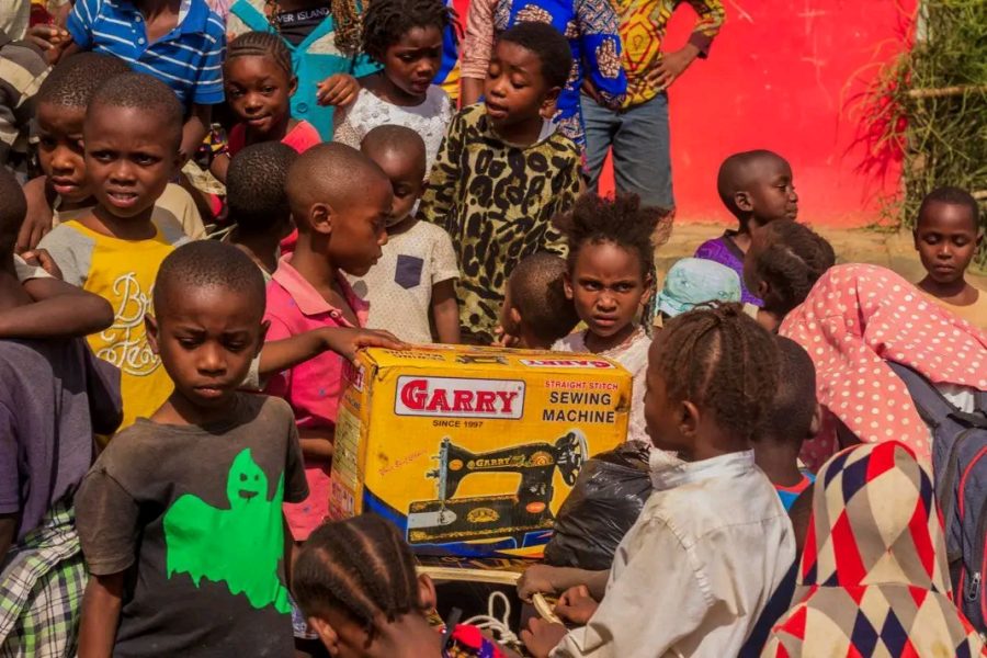 Children in Iziragobi community gathered around a sewing machine delivered for the She Means Business programme