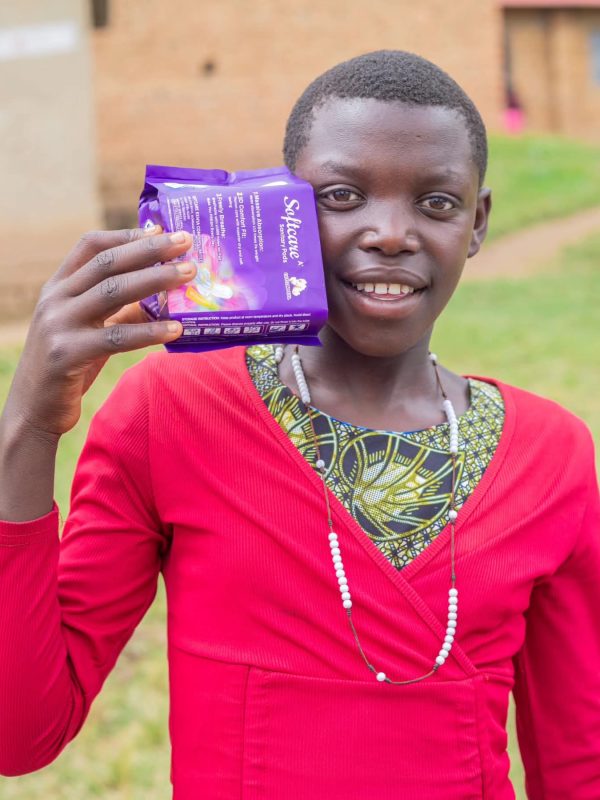 A smiling schoolgirl holding a pack of sanitary pads received through PPG menstrual health support